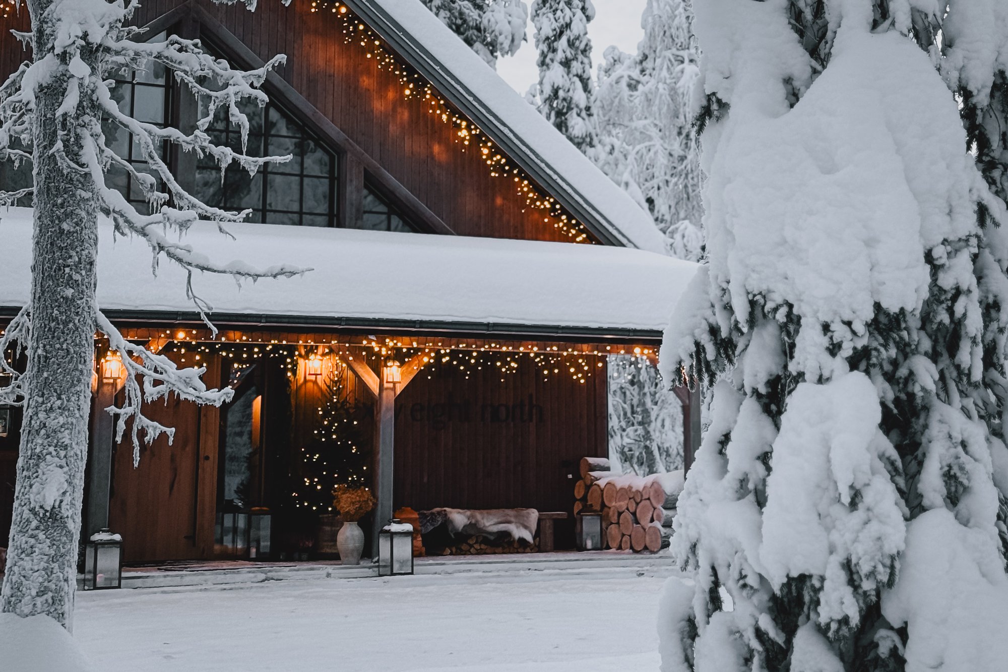 The lodge at Sixty Eight North lit with warm lanterns and fairy lights, surrounded by deep snow and frosted pines on a winter evening near Levi.